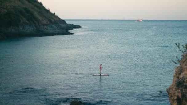 Mulher de fato de banho vermelho em SUP stand up paddle board em uma baía ao pôr do sol — Vídeo de Stock