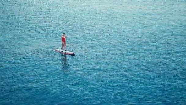 Mujer en traje de baño rojo en SUP de pie tabla de paddle en una bahía al atardecer — Vídeos de Stock