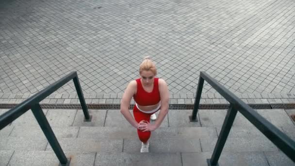 Plusz méretű vegyes verseny szőke mosolygós nő visel piros sportruházat bemelegítő futtatása előtt