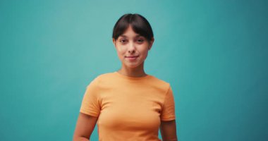 Neşeli İspanyol kadın mavi arka planda parlak bir gülümsemeyle kalp sembolü gösteriyor. Kadın, sevgiyi anlamlı jestlerle gösterir. Yavaş çekim