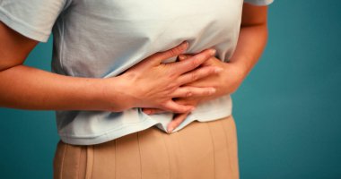 Mavi arka planda karın ağrısı çeken genç İspanyol kadın. Acı çeken Latin bir kadın stüdyoda ağır çekimde duruyor.