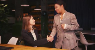 Genç iş kadınları toplantıda el sıkışıyor ve sözleşmenin ayrıntıları hakkında konuşuyorlar. Resmi takım elbiseli girişimciler iş anlaşmasının temel şartlarını netleştirdiler