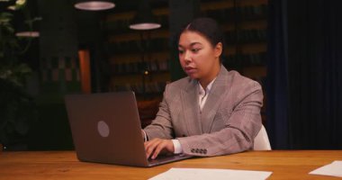 İş kadını ofisinde oturuyor ve laptopta odaklanmış bir ifadeyle çalışıyor. Ofis çalışanı dizüstü bilgisayardaki dijital sunumu dikkatlice düzenler