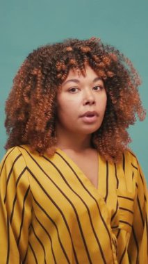 Üzgün genç İspanyol komik bir şekilde terleyerek yorgun olduğunu ve mavi arka planda hayal kırıklığına uğradığını gösteriyor. Duygusal çöküntüye uğramış Latin bir kadın stüdyoda ağır çekimde duruyor