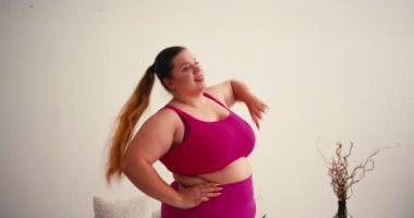 Kendine güveni tam kilolu kilolu kadın modern oturma odasında kol esnetme hareketleri yapıyor. Kadın, vücut pozitifliğini ve sağlıklı yaşam tarzını benimser.