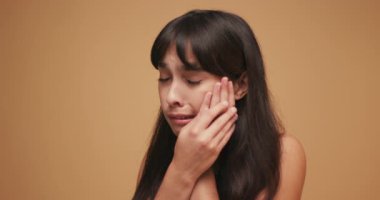 Mavi arka planda diş ağrısı hisseden genç Latin bir kadın. Acı çeken Latin bir kadın stüdyoda ağır çekimde duruyor.