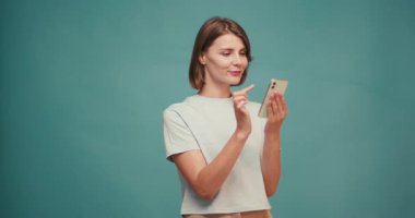 Sarı tişört giyen güzel genç bayan mavi arka planda sıcak bir şekilde gülümsüyor. Esmer, Latin bir kadın stüdyoda iyi hisler besliyor. Yavaş çekim