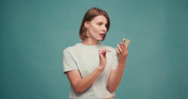 İspanyol kadın el sallıyor ve mavi arka plandaki akıllı telefonu kullanarak görüntülü konuşuyor. Kadın dalgaları görüntülü konuşma sırasında mutlu oluyor. Yavaş çekim