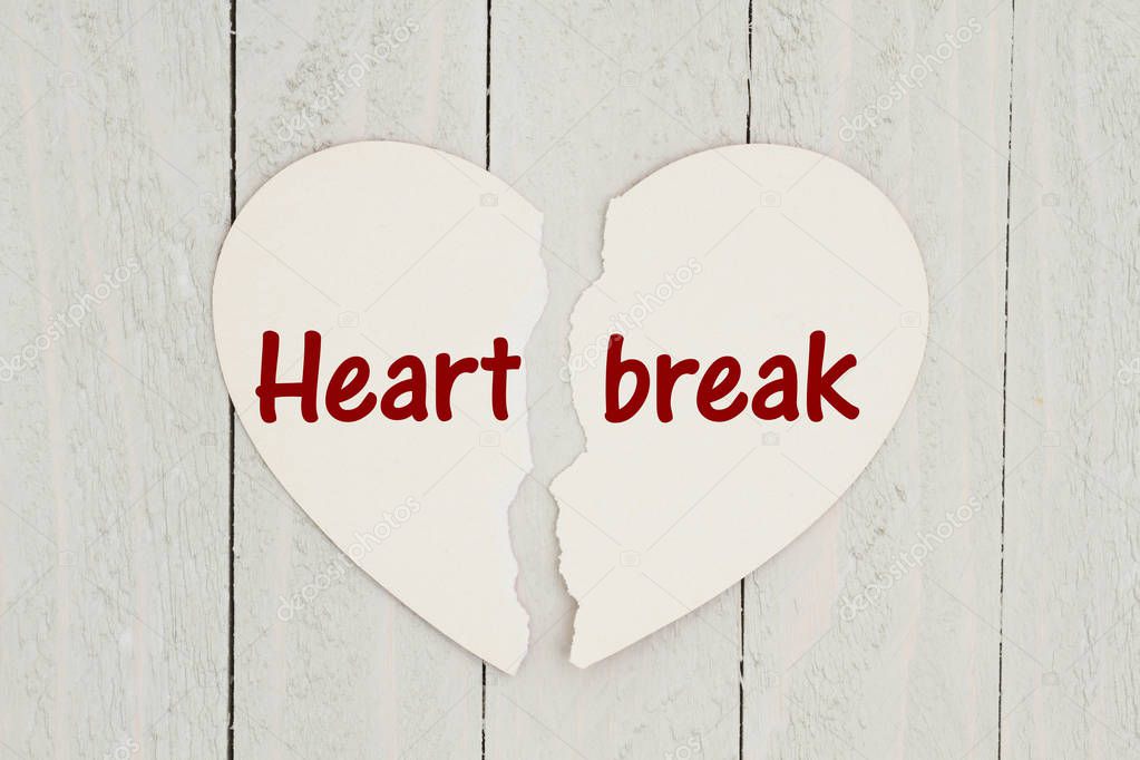 Torn heart-shape card on weathered wood background with text Heartbreak