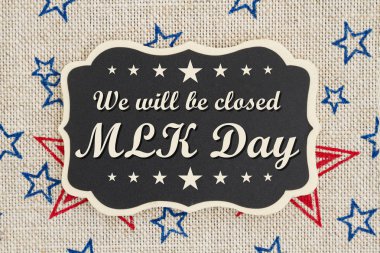 We will be closed MLK Day text on a chalkboard with patriotic USA red and blue stars on burlap