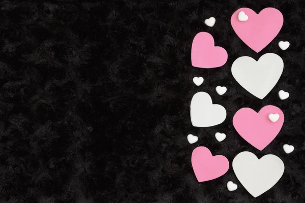 White and pink hearts with candy hearts on black rose textured plush fabric with copy space for your message