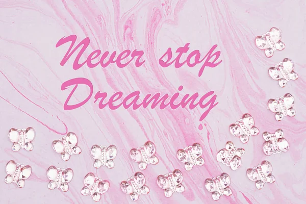 Сообщение Never Stop Dreaming с розовыми стеклянными бабочками на розовом фоне — стоковое фото