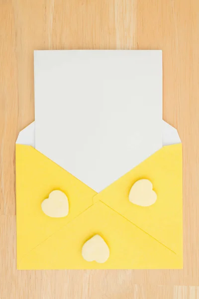 Envelope amarelo em branco com nota branca em branco em uma mesa com coração — Fotografia de Stock