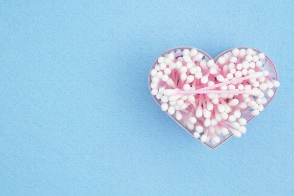 Bílé a růžové bavlněné tampony v kontejneru srdce na modré papírové b — Stock fotografie
