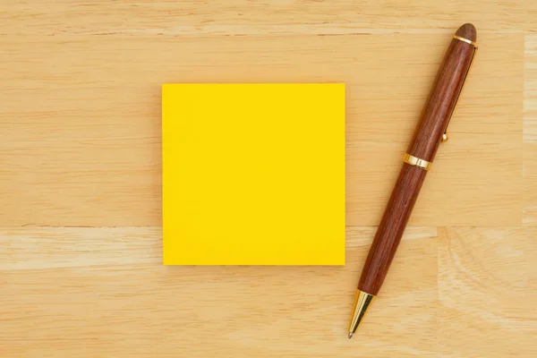 Gele lege kleverige nota met een pen op getextureerde houten achtergrond — Stockfoto