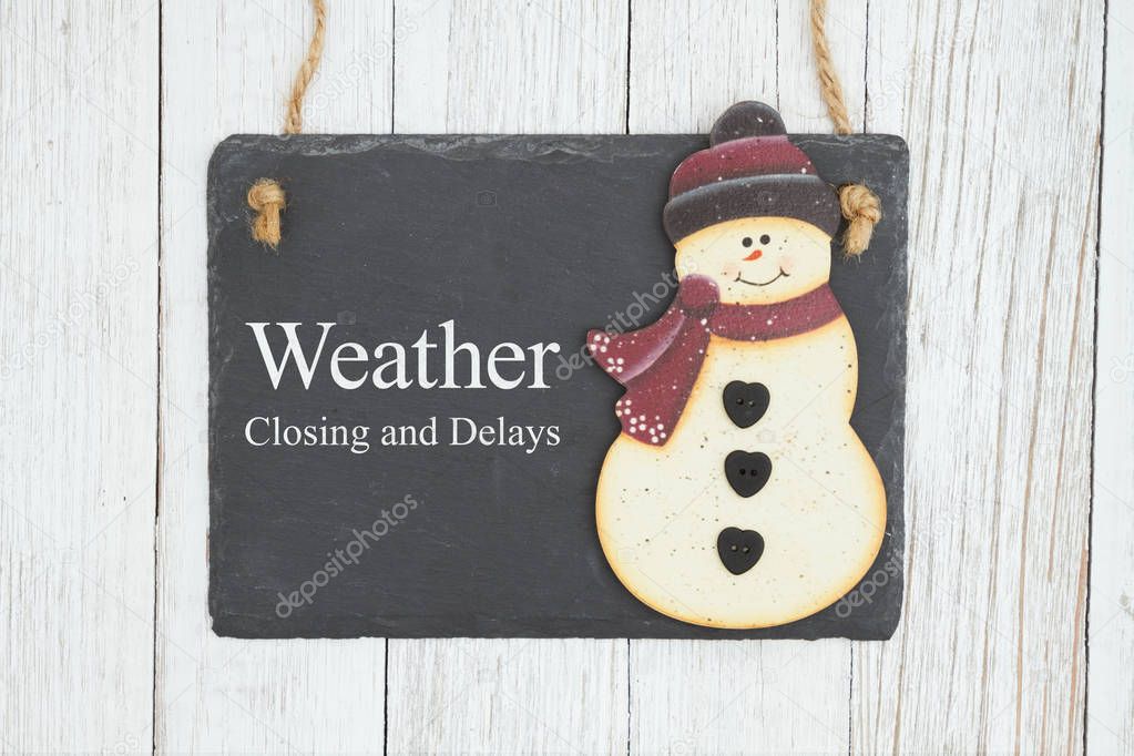 Weather closing and delays sign on a hanging chalkboard with sno