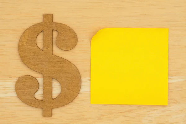 Yellow blank sticky note with a dollar sign on textured wood des — 스톡 사진