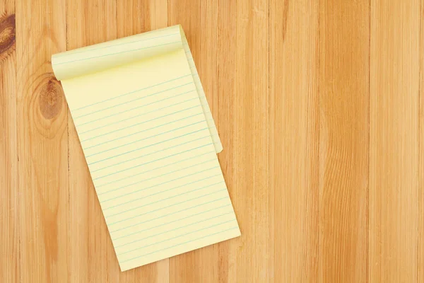 Yellow legal notepad paper with lines on pine wood desk with copy space for your business or writing message or mockup