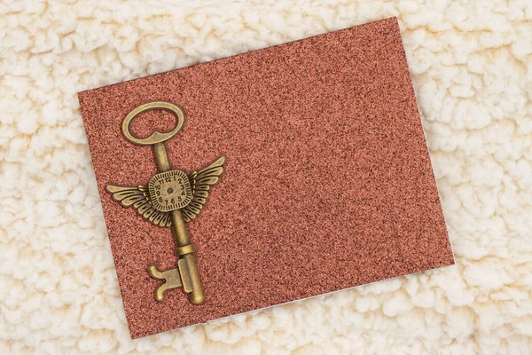 Blank brown glitter greeting card bronze skeleton key on beige plush fabric mockup with copy space for fall or time message