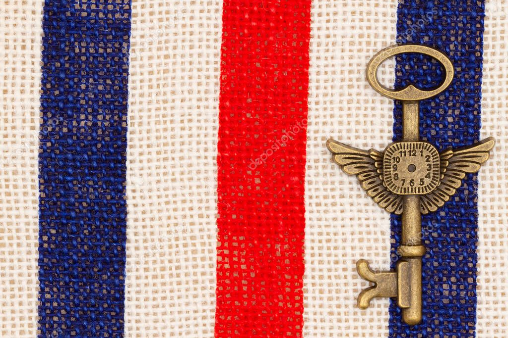 Bronze metal time skeleton key on red, white and blue grunge burlap textured weave material 