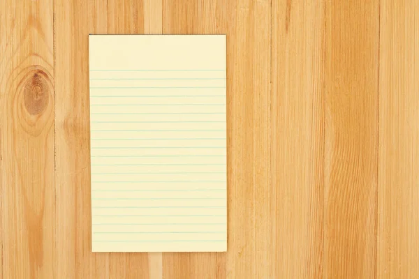 Yellow legal notepad paper with lines on pine wood desk with copy space for your business or writing message or mockup