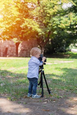 İki yıl yaşlı erkek çocuk fotoğrafçıdır. Çocuk bir fotoğraf makinesi tripod üzerinde tutan ve manzara fotoğrafı çeker. Küçük çocuk gömlek ve parkta oynarken kot giymiş.