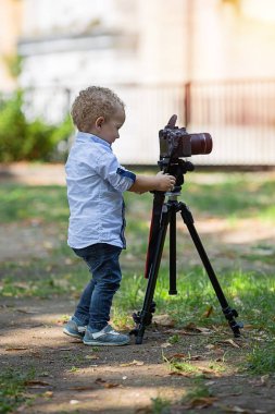 İki yıl yaşlı erkek çocuk fotoğrafçıdır. Çocuk bir fotoğraf makinesi tripod üzerinde tutan ve manzara fotoğrafı çeker. Küçük çocuk gömlek ve parkta oynarken kot giymiş.