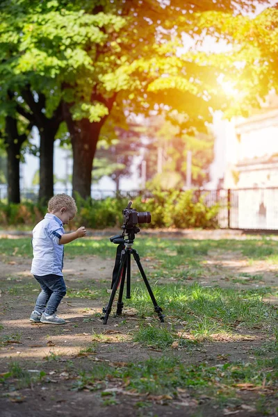 年歳の少年は 写真家です 子供は 三脚にカメラを保持しているし 風景の写真を取る 小さな子供服シャツとジーンズが公園で遊んで — ストック写真