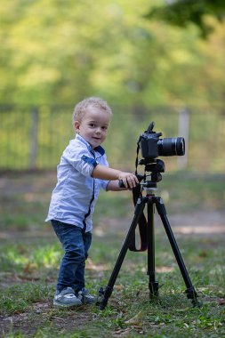 İki yıl yaşlı erkek çocuk fotoğrafçıdır. Çocuk bir fotoğraf makinesi tripod üzerinde tutan ve manzara fotoğrafı çeker. Küçük çocuk gömlek ve parkta oynarken kot giymiş.