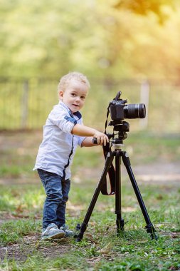 İki yıl yaşlı erkek çocuk fotoğrafçıdır. Çocuk bir fotoğraf makinesi tripod üzerinde tutan ve manzara fotoğrafı çeker. Küçük çocuk gömlek ve parkta oynarken kot giymiş.