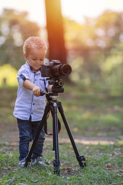 İki yıl yaşlı erkek çocuk fotoğrafçıdır. Çocuk bir fotoğraf makinesi tripod üzerinde tutan ve manzara fotoğrafı çeker. Küçük çocuk gömlek ve parkta oynarken kot giymiş.