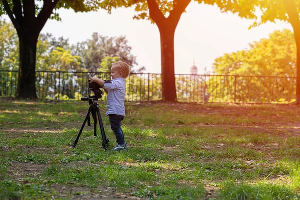 年歳の少年は 写真家です 子供は 三脚にカメラを保持しているし 風景の写真を取る 小さな子供服シャツとジーンズが公園で遊んで — ストック写真