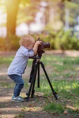 İki yıl yaşlı erkek çocuk fotoğrafçıdır. Çocuk bir fotoğraf makinesi tripod üzerinde tutan ve manzara fotoğrafı çeker. Küçük çocuk gömlek ve parkta oynarken kot giymiş.