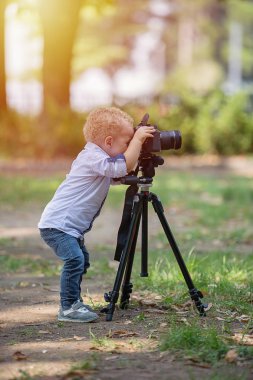İki yıl yaşlı erkek çocuk fotoğrafçıdır. Çocuk bir fotoğraf makinesi tripod üzerinde tutan ve manzara fotoğrafı çeker. Küçük çocuk gömlek ve parkta oynarken kot giymiş.