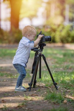 İki yıl yaşlı erkek çocuk fotoğrafçıdır. Çocuk bir fotoğraf makinesi tripod üzerinde tutan ve manzara fotoğrafı çeker. Küçük çocuk gömlek ve parkta oynarken kot giymiş.