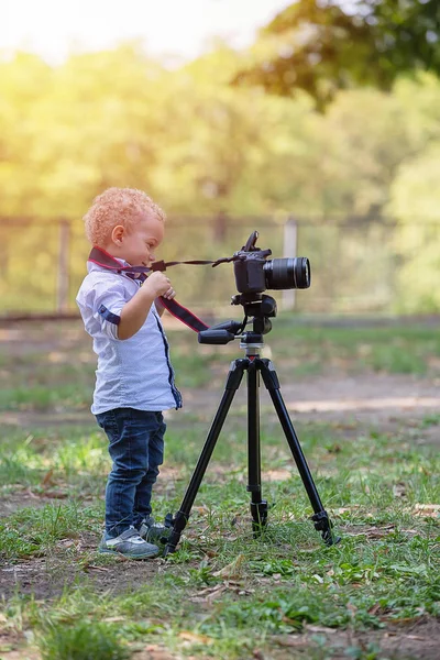 İki yıl yaşlı erkek çocuk fotoğrafçıdır. Çocuk bir fotoğraf makinesi tripod üzerinde tutan ve manzara fotoğrafı çeker. Küçük çocuk gömlek ve parkta oynarken kot giymiş.