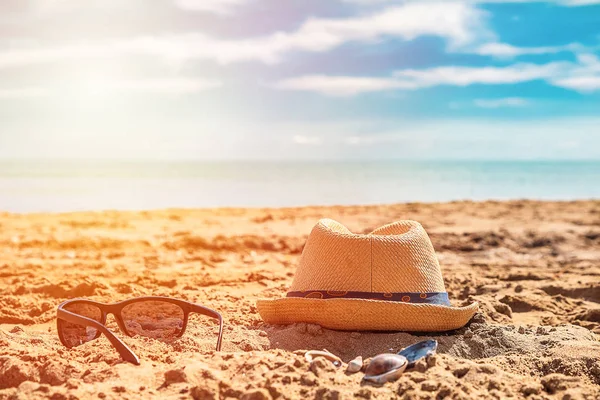 Sunglass and cap on sand against turquoise sea. Tourism and vacation concept on a tropical beach. Happy sunny day on beach.