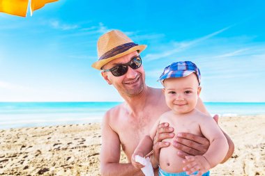 Baba ve oğul yaz sahilde oynarken gündüz. İnsanlar dışarıda eğleniyor. Yaz tatili ve dostu aile kavramı.