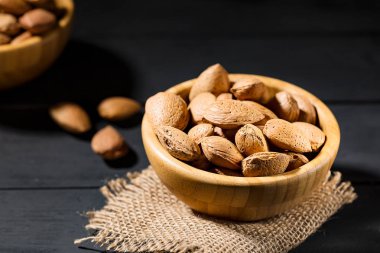 Bütün organik badem fındık kabuğu siyah masada ahşap bir kase ile. Seçici odak. Kopya alanı