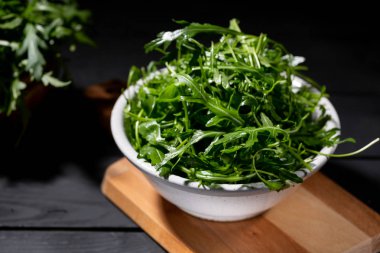 Roket salata tam ahşap kase taze rucola siyah arka plan üzerinde seçici odak bırakır