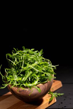 Roket salata tam ahşap kase taze rucola yaprakları siyah arka plan, seçici odak, kopya alanı üzerinde.