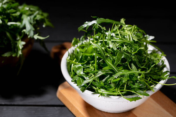 Fresh rucola in the wood bowl full of rocket salad leaves over the black background, selective focus