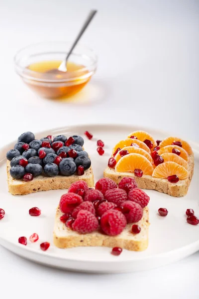 Sandwich with pomegranate grains, honey and berries over white background. Raw food. Healthy food for breakfast or lunch. Selective focus.