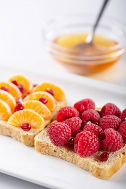 Nar taneleri, bal, mandalina ve beyaz arka plan üzerinde ahududu ile sandviç. Çiğ gıda. Kahvaltı ve öğle yemeği için sağlıklı yemek. Seçici odak.