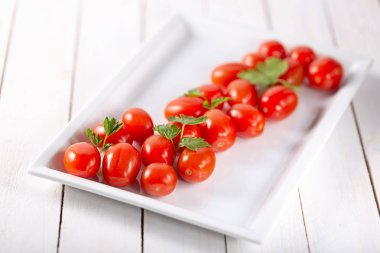 Beyaz ahşap zemin üzerinde seramik tabak içinde taze organik kiraz domates. Üstten Görünüm. Yat. Yumuşak odak.