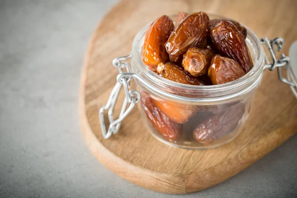 Dried dates in a glass jar on a light grey marble table.
