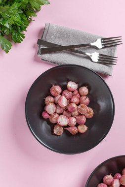 Beautiful roasted radishes in a black plate on pink table close up. clipart