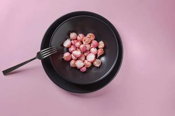 Όμορφα καβουρδισμένα ραπανάκια σε μαύρο πιάτο σε ροζ τραπέζι από κοντά. — Φωτογραφία Αρχείου