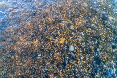 Deniz kumsalında küçük taşlar üzerinde deniz köpüğü yakın