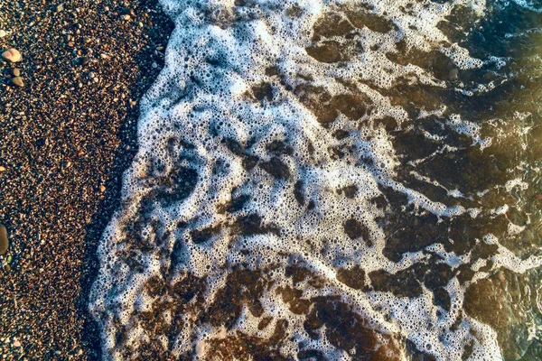 Espuma do mar em pequenas pedras na praia do mar de perto — Fotografia de Stock